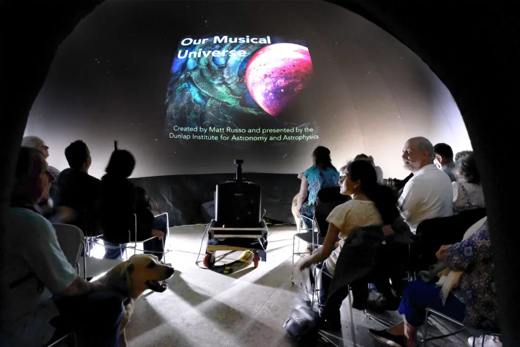 A group of people from the CNIB sitting inside the planetarium dome