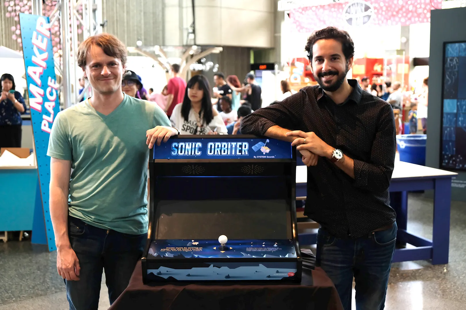 Matt and Andrew from System Sounds standing beside the Sonic Orbiter arcade machine